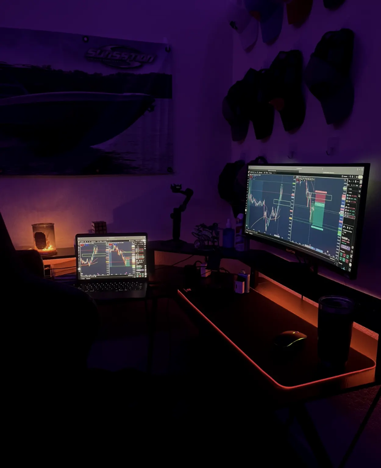 The TakeProfit HQ trading desk at night — a curved ultrawide monitor and a laptop showing charts, lit by the room’s LED lighting